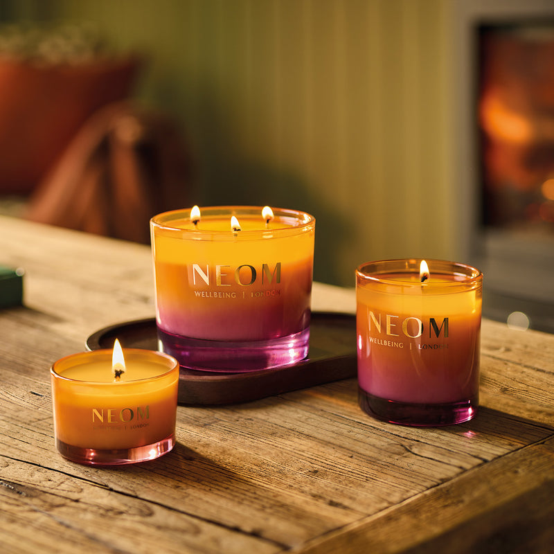 Three NEOM candles on a wooden surface with a warm glow.