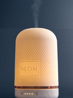 NEOM electric pod diffuser emitting steam on a dark background