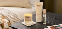 NEOM skincare products including a candle, body butter, and sleep mist on a table.