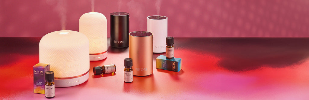 Collection of pod diffusers and essential oils on a reflective surface with a pink gradient background