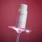 NEOM bottle on a pink stand against a red background