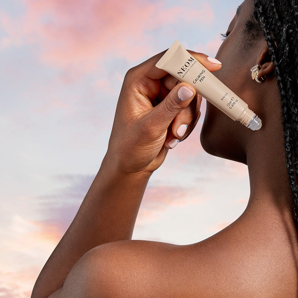 Person holding a NEOM Calming Pen against a blurred natural background