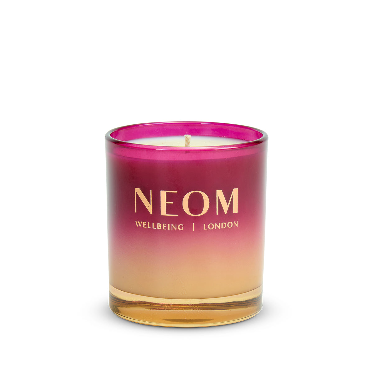 NEOM candle with a gradient pink to gold design on a white background