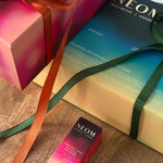 NEOM Christmas gift boxes wrapped with green and orange ribbons beside Christmas Wish Essential Oil Blend.