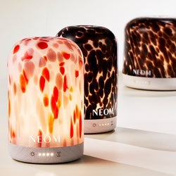Three NEOM pod electric diffusers with different designs on a white surface.
