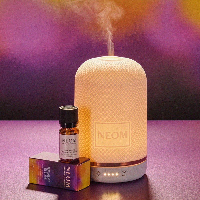 Neom diffuser and essential oil bottle on a purple background