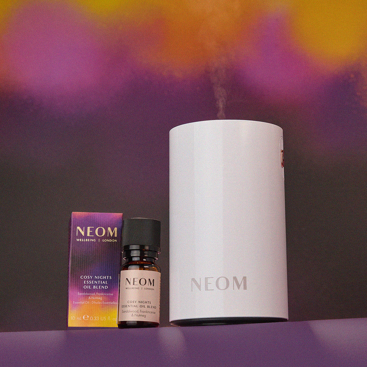 NEOM diffuser, essential oil blend, and oil bottle on a purple background