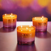 Three NEOM candles on a reflective surface with a blurred colorful background