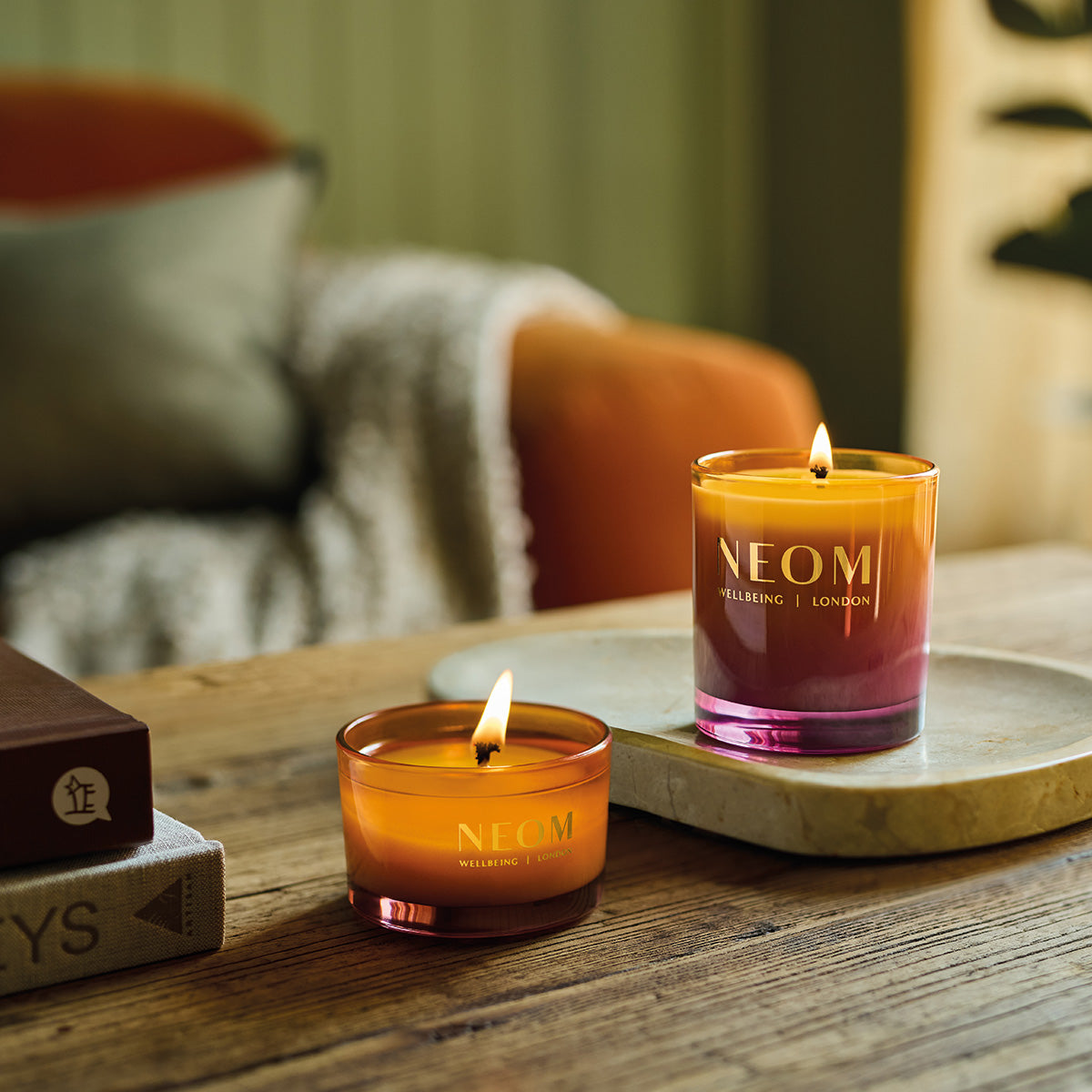 Two NEOM candles on a wooden surface with a blurred background