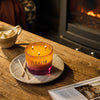 NEOM candle on a wooden table with a fireplace in the background