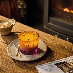 NEOM candle on a wooden table with a fireplace in the background