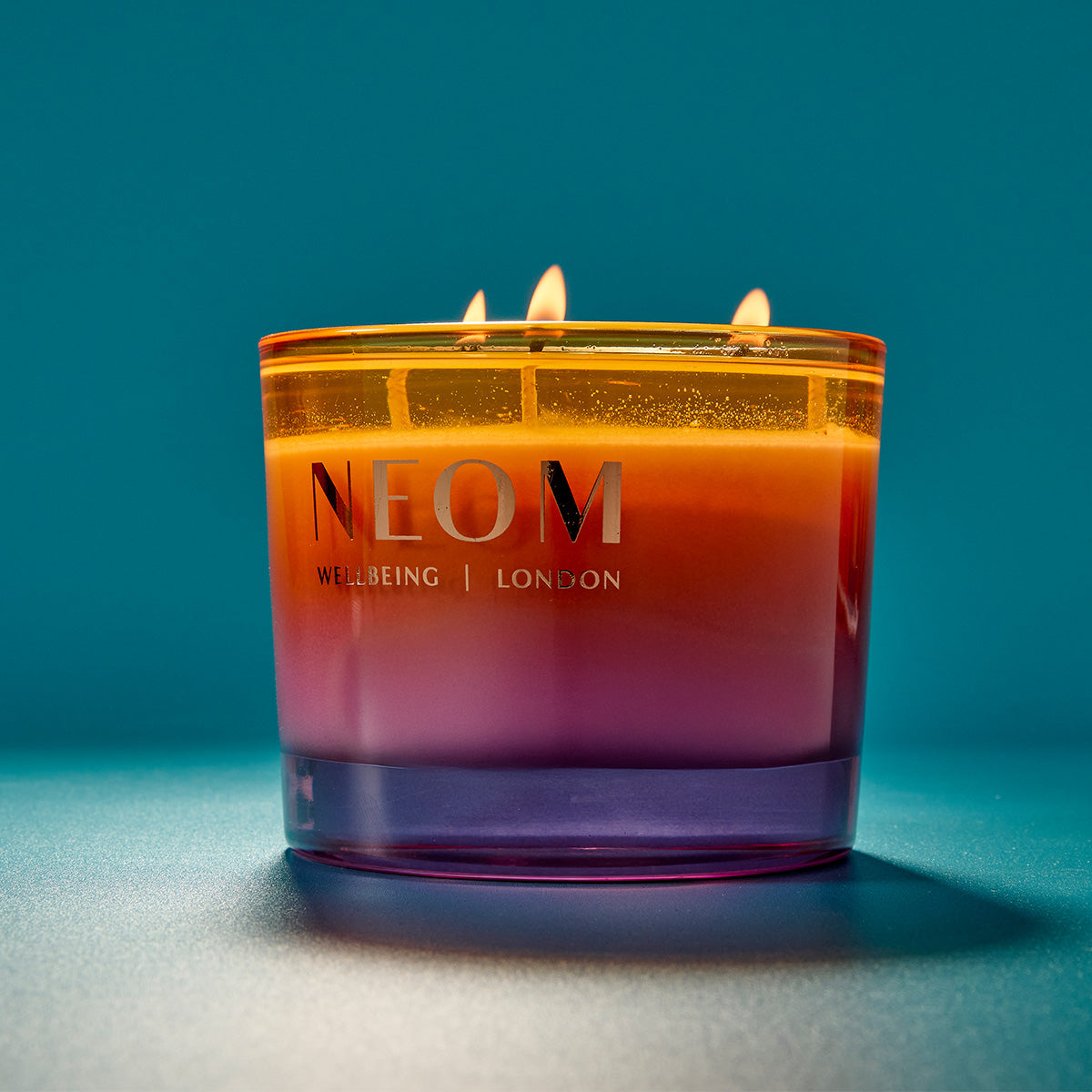 NEOM candle with a gradient colour on a blue background