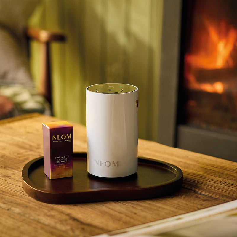 NEOM diffuser and box on a wooden table with a fireplace in the background