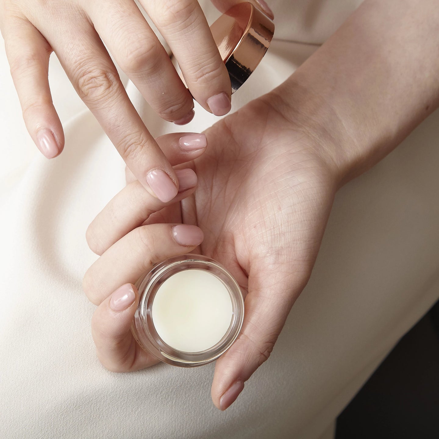 Close-up of hands holding a wonder balm with a beige background