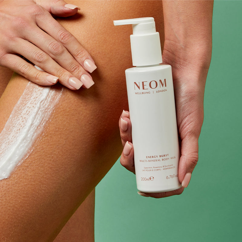 Person applying NEOM body milk to their arm with a green background