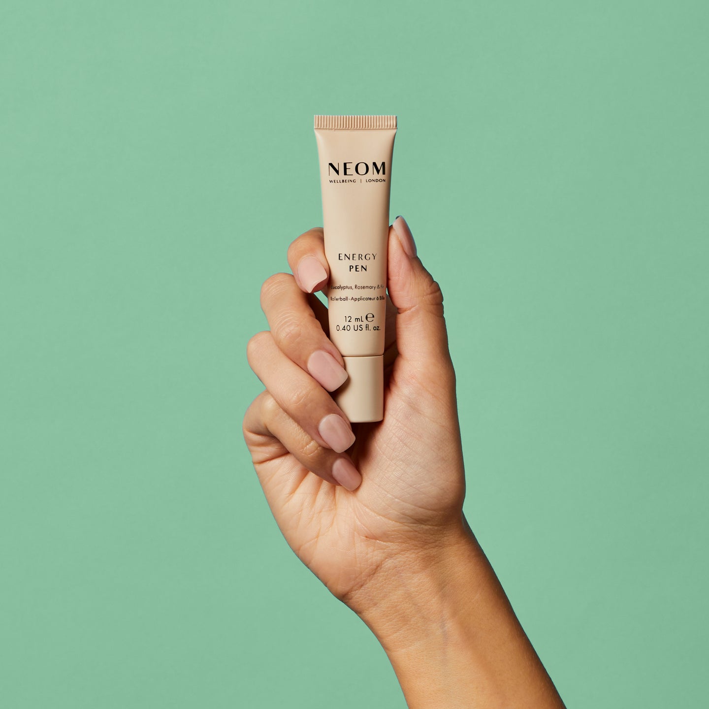 Hand holding a NEOM Energy Pen  against a green background