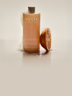NEOM Great Day exfoliating body wash with wild mint and mandarin beside fresh orange slice