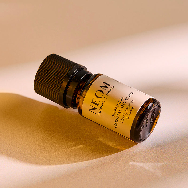 NEOM Happiness essential oil blend bottle lying on a softly lit surface.