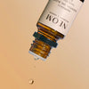 Close-up of an NEOM Happiness essential oil bottle releasing a drop of oil against a neutral background.