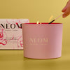 NEOM candle being lit with a box in the background on a yellow background