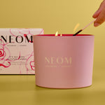 NEOM candle being lit with a box in the background on a yellow background