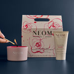 NEOM candle, hand balm, and packaging on a dark background