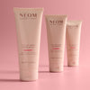Three Neom hand balms on a pink background