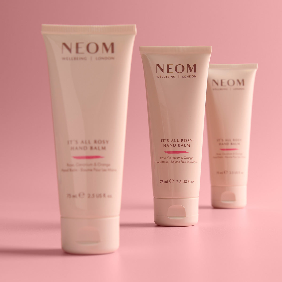 Three Neom hand balms on a pink background
