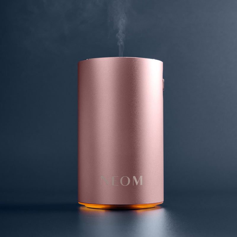 Pink NEOM diffuser emitting steam on a dark background
