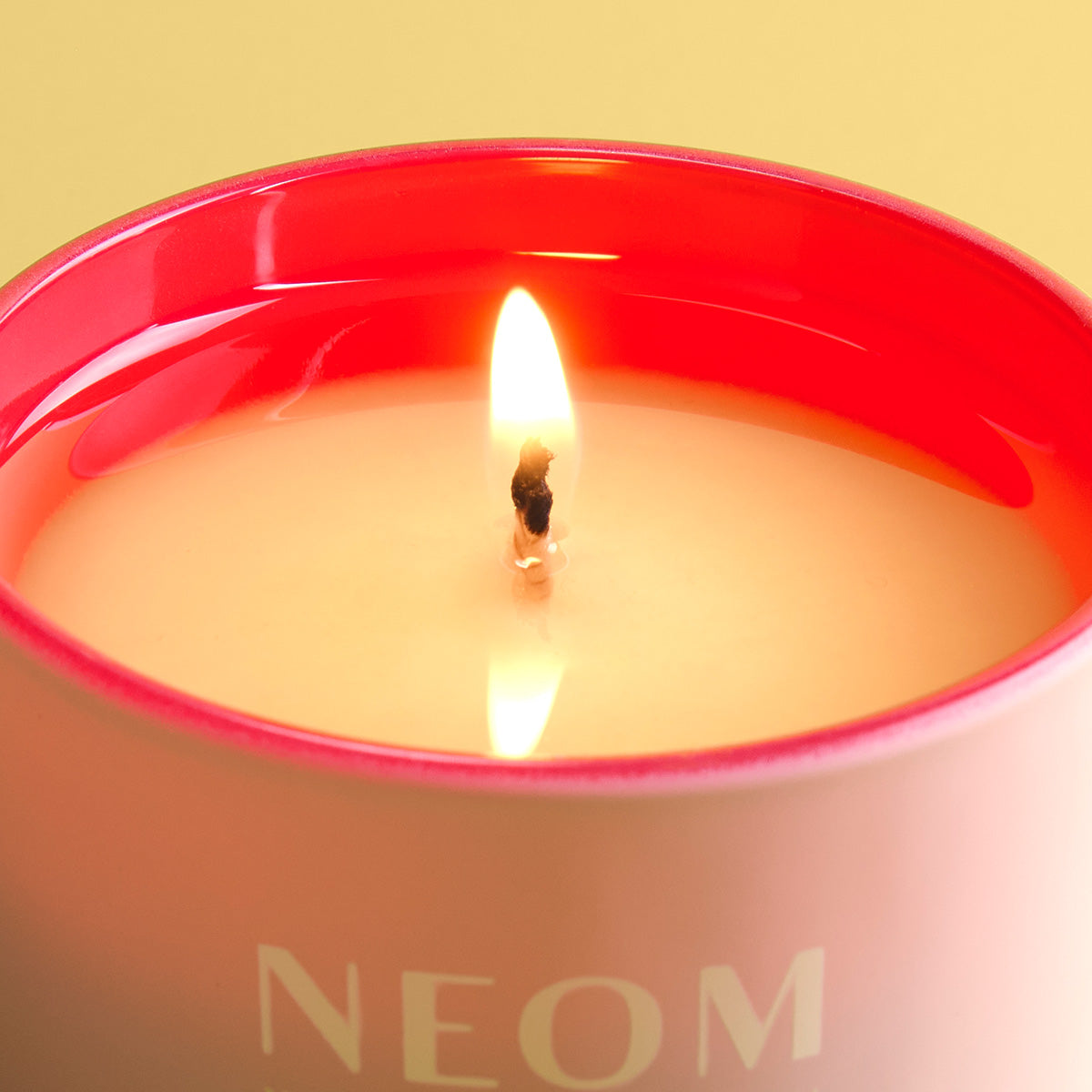 Candle with a red rim and 'NEOM' branding on a yellow background