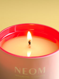 NEOM candle with a lit flame on a yellow background