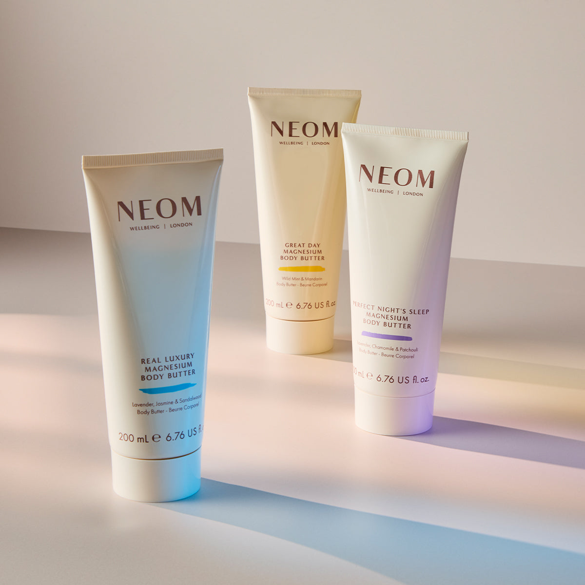 Three NEOM magnesium body butter skincare products on a gradient background