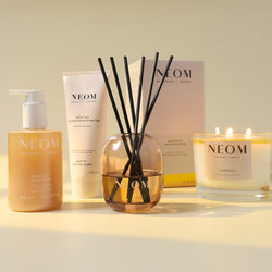 NEOM product lineup including a bottle, tube, diffuser, and candle on a light background