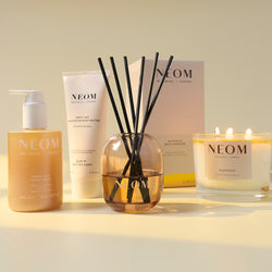 NEOM product lineup including a hand wash, body butter, reed diffuser, and candle on a light background