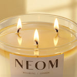 NEOM three-wick luxury scented candle with warm glowing flames.