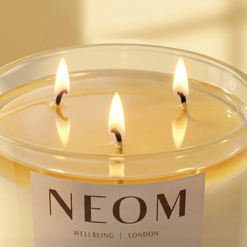 NEOM three-wick luxury scented candle with warm glowing flames.