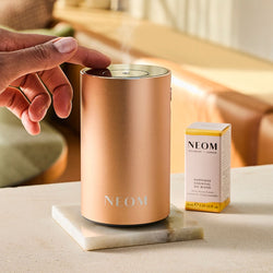 Hand activating NEOM gold Wellbeing Pod luxury essential oil diffuser.