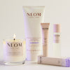 NEOM skincare and wellness products including a candle, body butter, pillow mist and sleep pen on a light background.