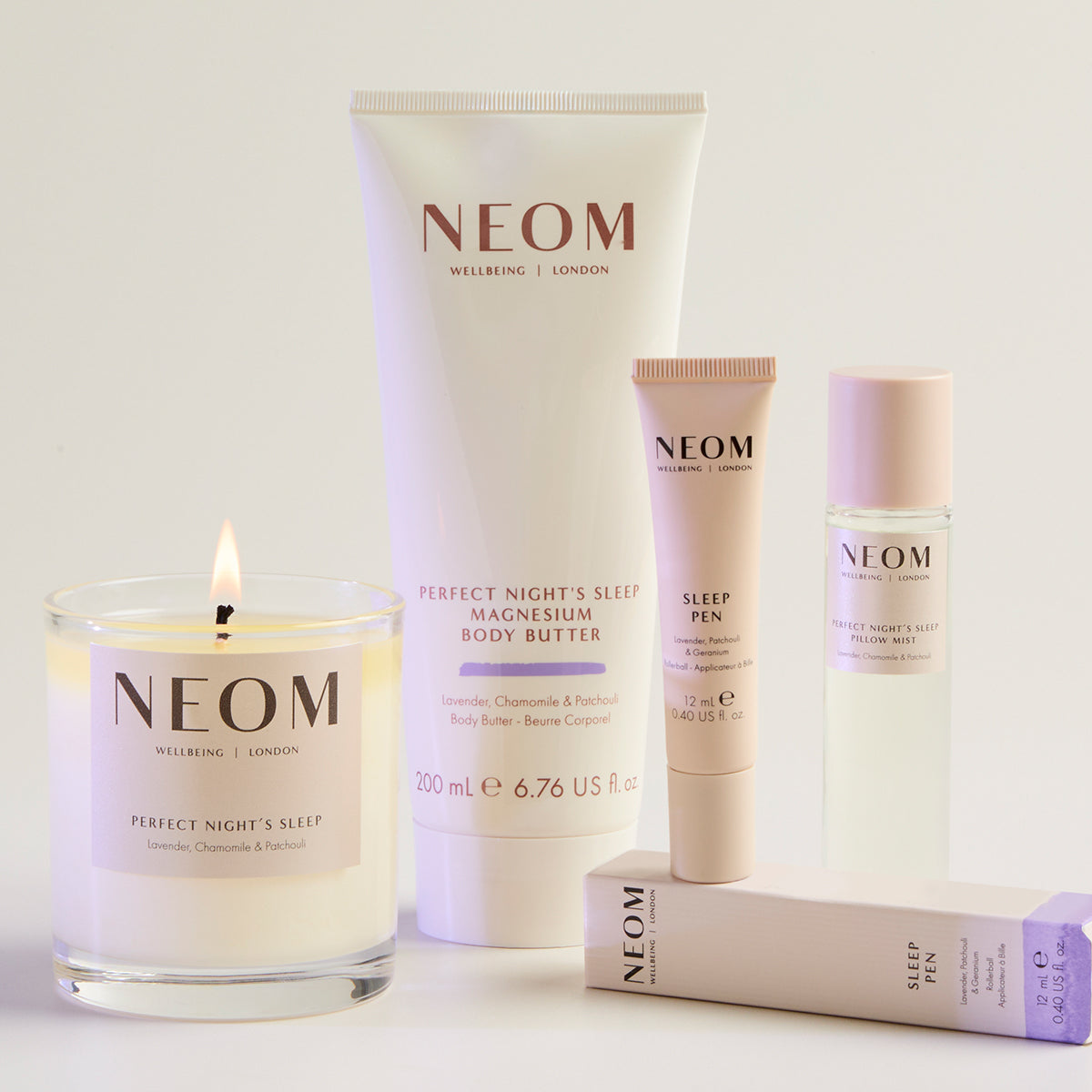 NEOM skincare and wellness products including a candle, body butter, pillow mist and sleep pen on a light background.