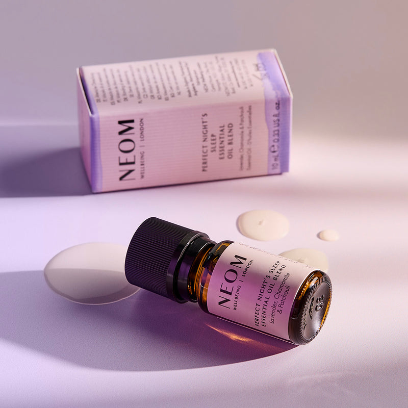 NEOM Perfect Night’s Sleep essential oil blend bottle lying beside its box with oil droplets on the surface.