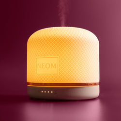 NEOM electric pod luxe diffuser emitting steam on a dark purple 