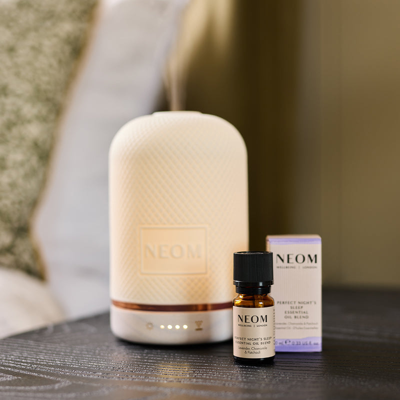 NEOM diffuser and essential oil bottles on a table with a blurred background