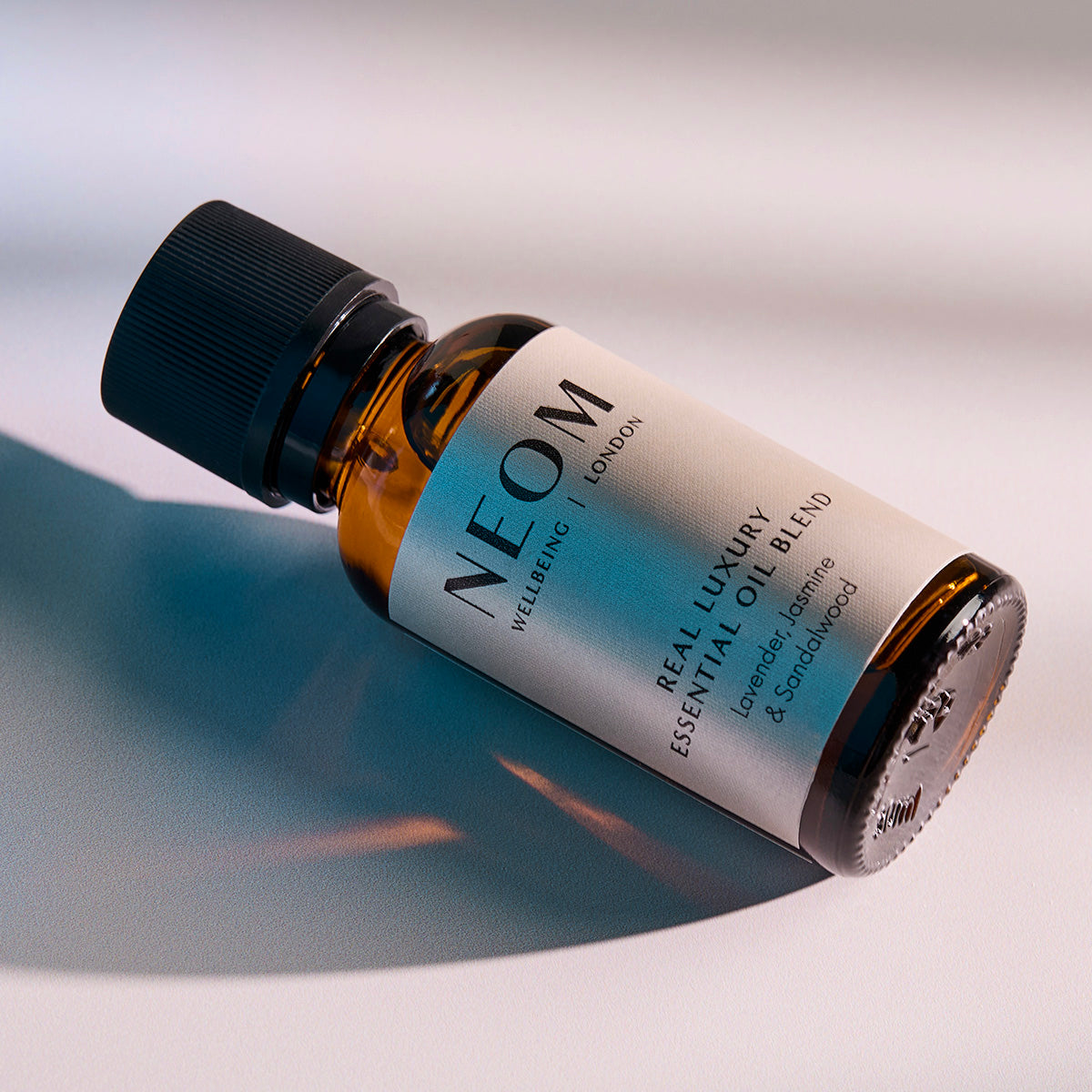 NEOM Real Luxury essential oil blend bottle lying on a surface with soft shadows.