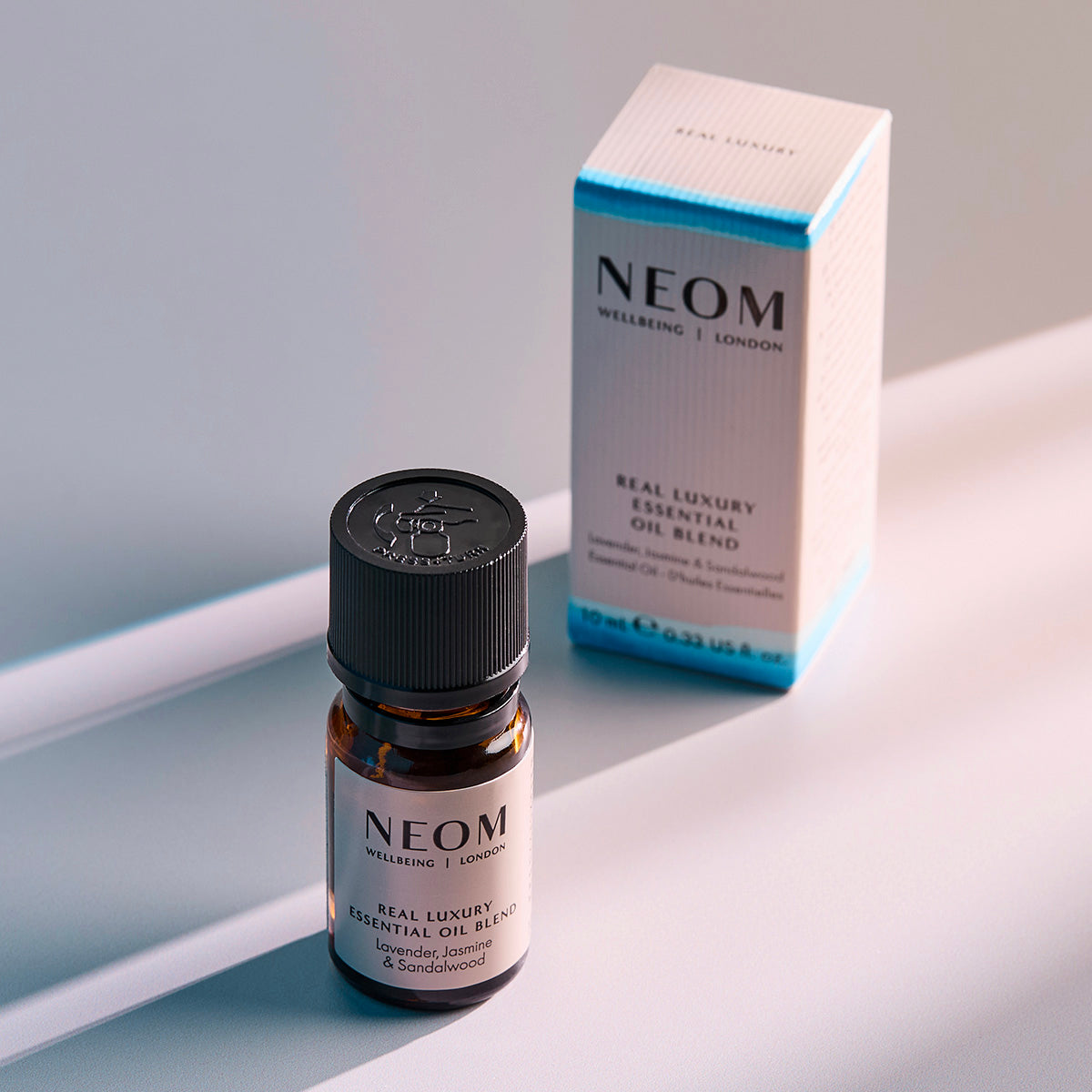 NEOM Real Luxury essential oil blend bottle standing beside its product box on a softly lit surface.