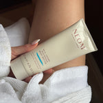 a person holding NEOM real luxury magnesium body butter on their leg in a dressing gown