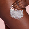 Hand applying a cream or lotion to a person's skin on a pink background