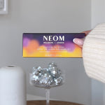 Hand holding NEOM Scent the Season Discovery Set box with essential oil blends and silver disco balls.
