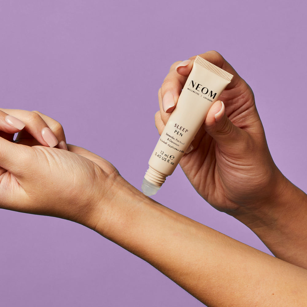 Person applying NEOM Sleep Pen to their arm against a purple background