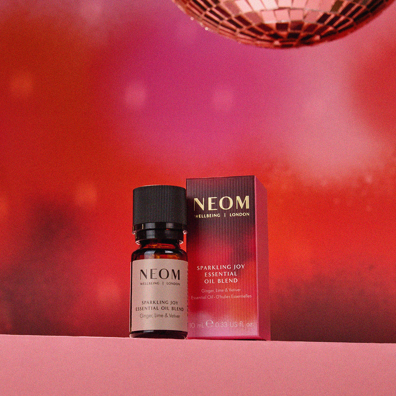 NEOM essential oil bottle and packaging on a red background with disco ball
