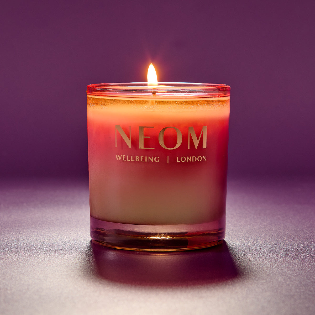 NEOM candle with a purple gradient on a matching background